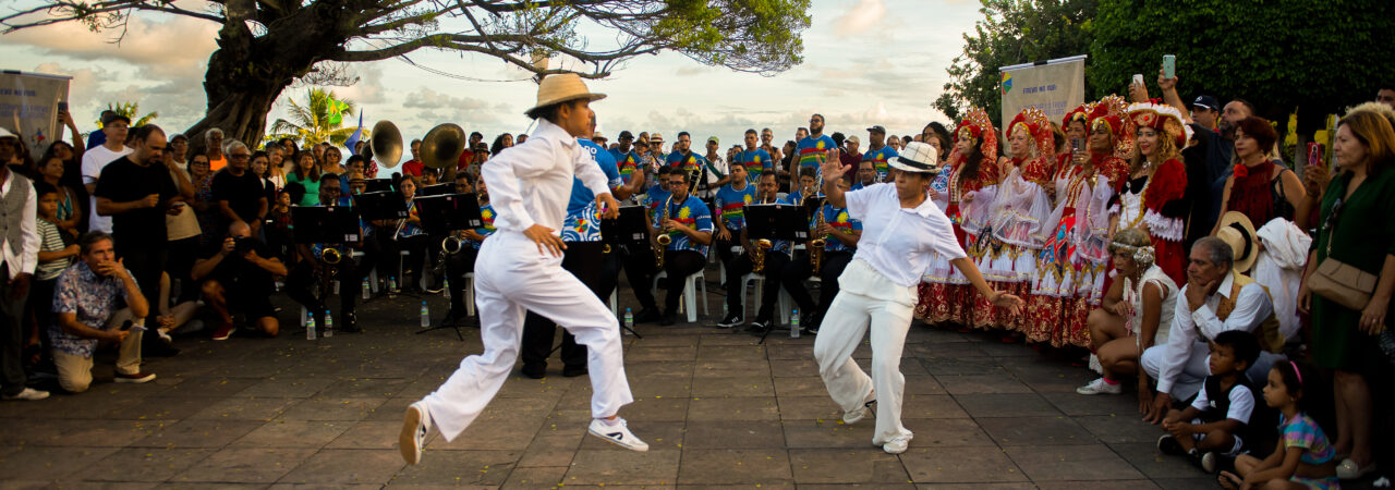 Dois passistas dançando frevo próximo ao pôr-do-sol