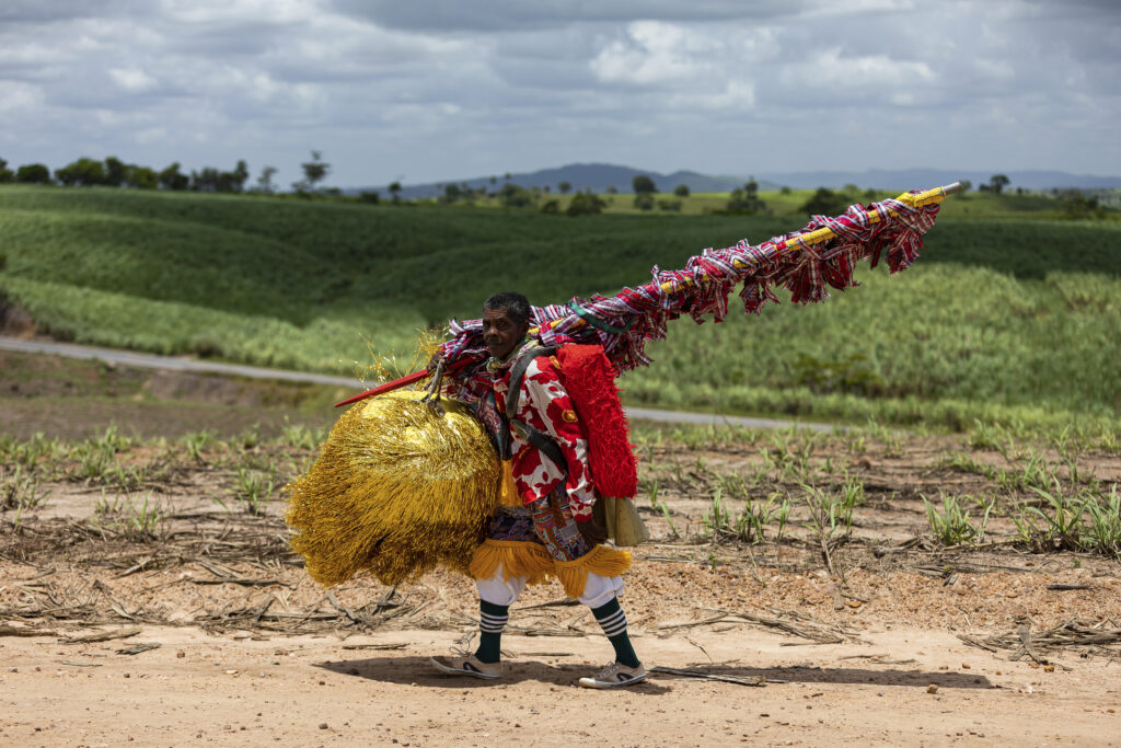 Fotografia de um caboclo de lança, personagem do Maracatu Rual de Pernaambuco, andando em um canavial.